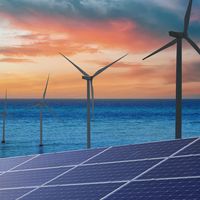 Composite image showing solar panels in the foreground and offshore wind turbines in the ocean at sunset, representing alternative energy sources.